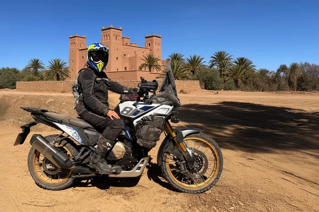 Escena de motorista subido en una moto trail blanca junto a una Kasbah en Merzouga