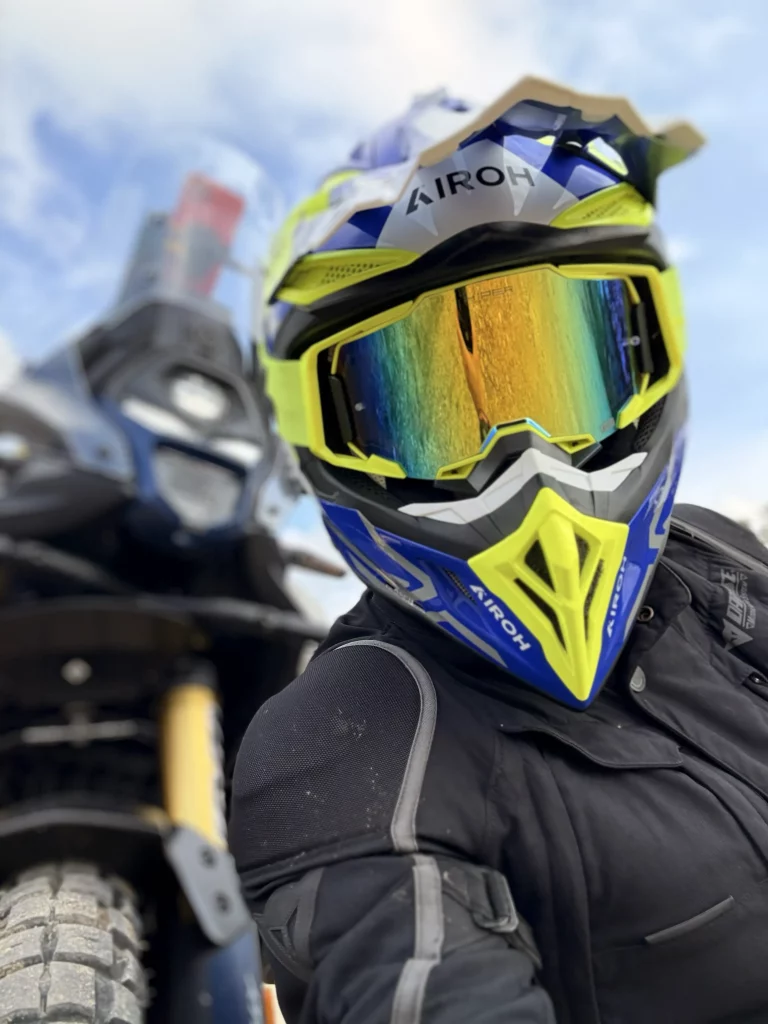 Motorista con un casco azul y amarillo AIROH AVIATOR y gafas de enduro 100%